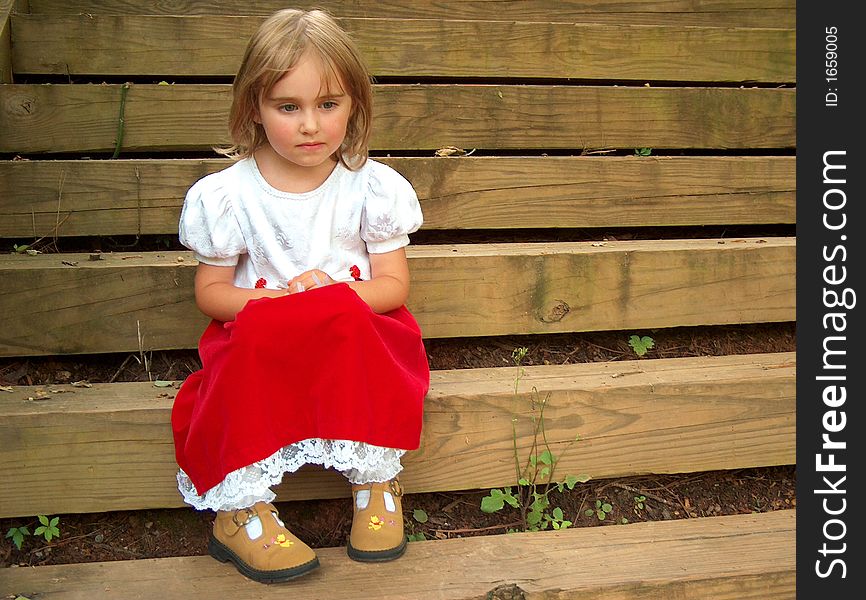 Little girl in red dress sitting on steps thinking