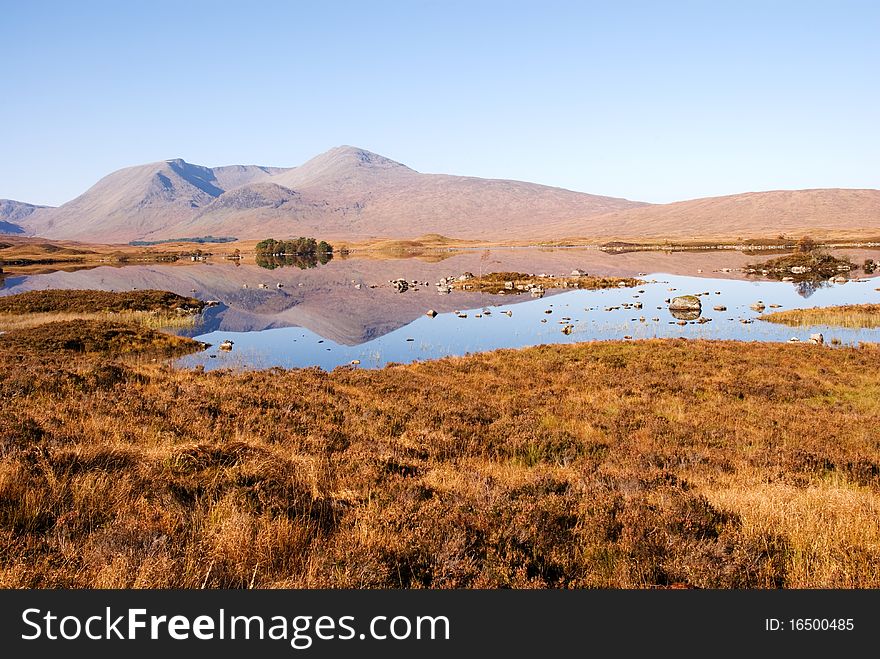 A horizontal image of the mountains on the Rannoch Moor in the Scottish Highlands reflecting on the water