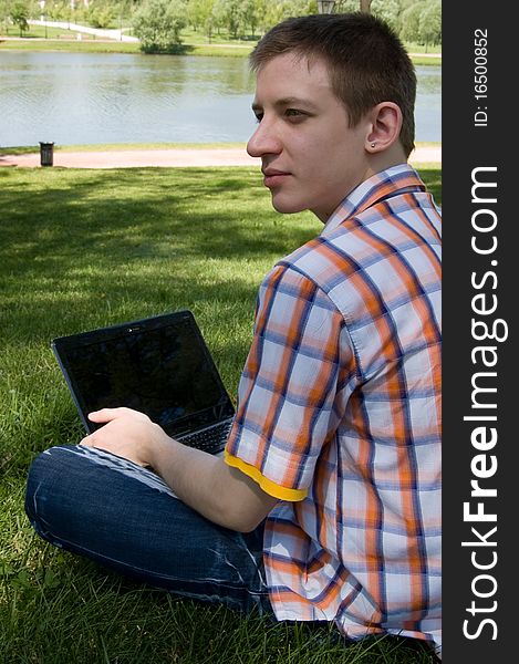 Young man sitting on green grass in park and types on laptop. Young man sitting on green grass in park and types on laptop