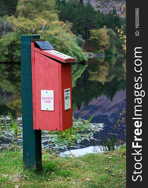 A vertical image of a safety line box beside a loch with autumn reflections