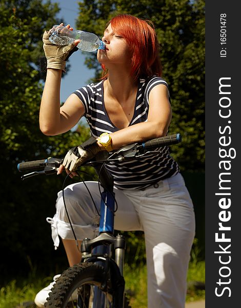 Adult smiling biker woman on mounting bike drinking mineral water. Adult smiling biker woman on mounting bike drinking mineral water