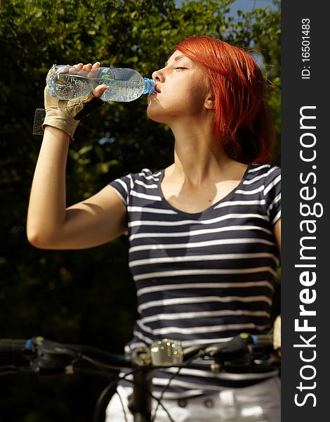 Adult smiling biker woman on mounting bike drinking mineral water. Adult smiling biker woman on mounting bike drinking mineral water