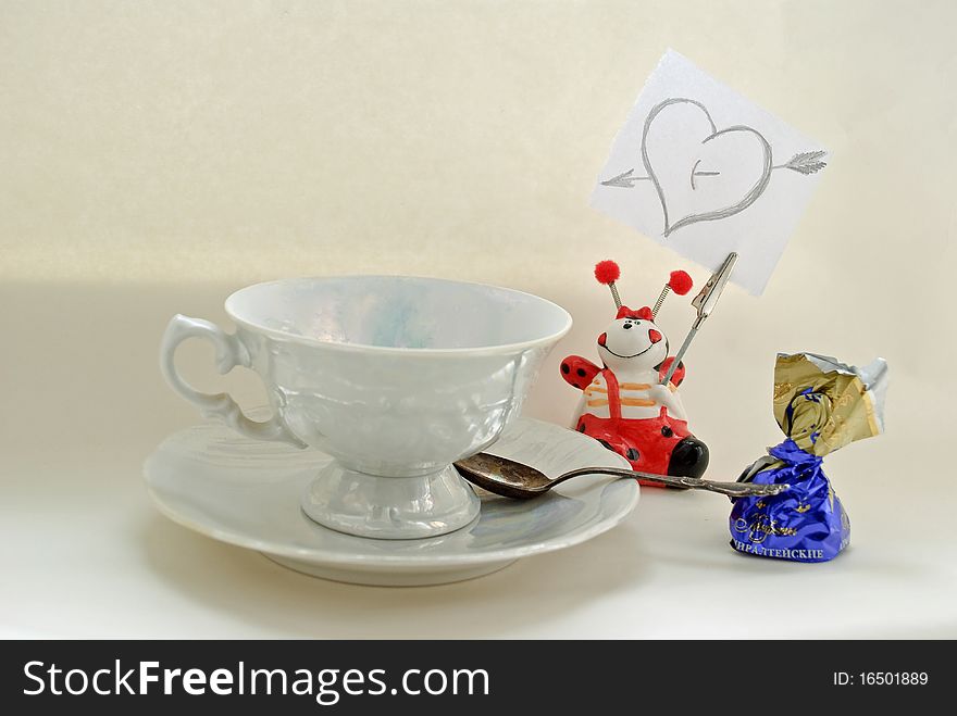 White cup, spoon, candy, aucer and note with heart at the white background. White cup, spoon, candy, aucer and note with heart at the white background