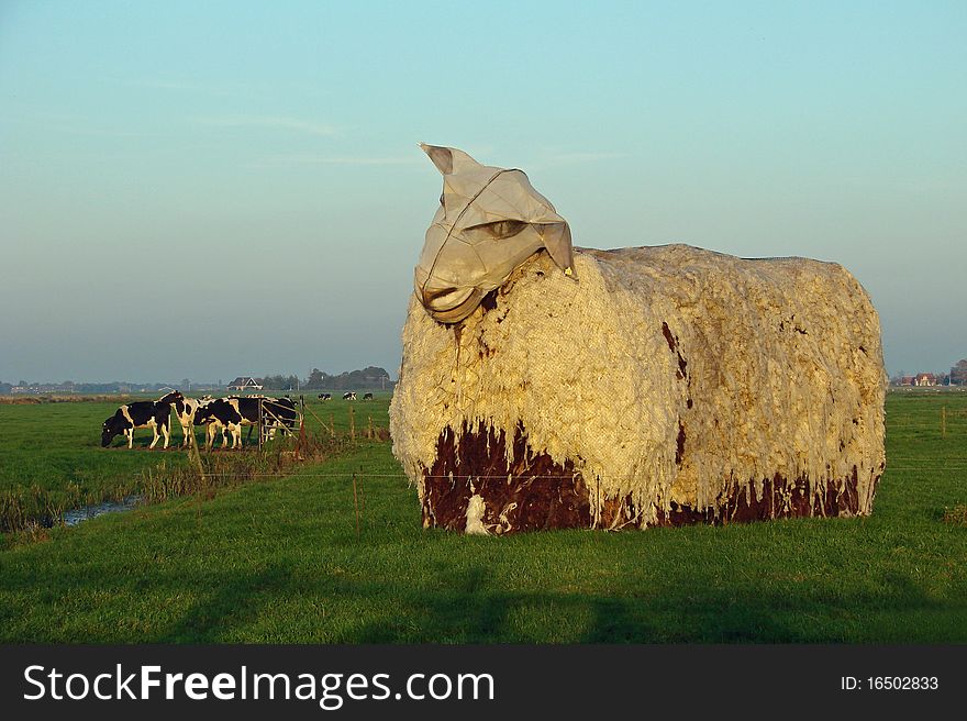 Giant sheep statue in the afternoon sun, with a cows in the background, photo taken in the Netherlands. Giant sheep statue in the afternoon sun, with a cows in the background, photo taken in the Netherlands