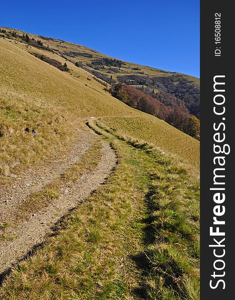 Soil road on a hillside in an autumn landscape with the dark blue sky. Soil road on a hillside in an autumn landscape with the dark blue sky.