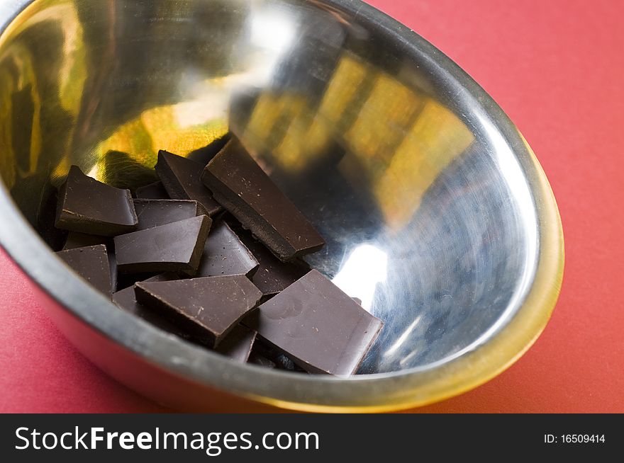 Crushed dark chocolate in a cooking bowl over red background