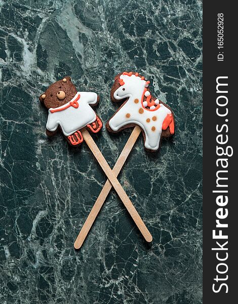 Cookies bear and horse on the stick on green marble background view from above
