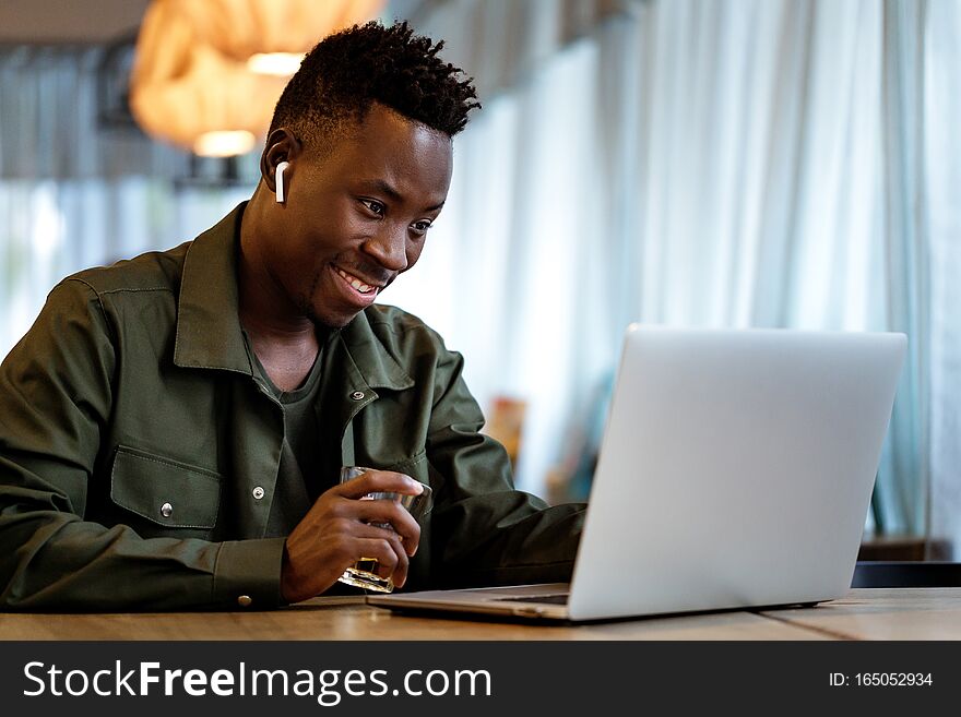 Cheerful african american man in headphones using computer in cafe. young smiling businessman working on laptop. copy space. Cheerful african american man in headphones using computer in cafe. young smiling businessman working on laptop. copy space