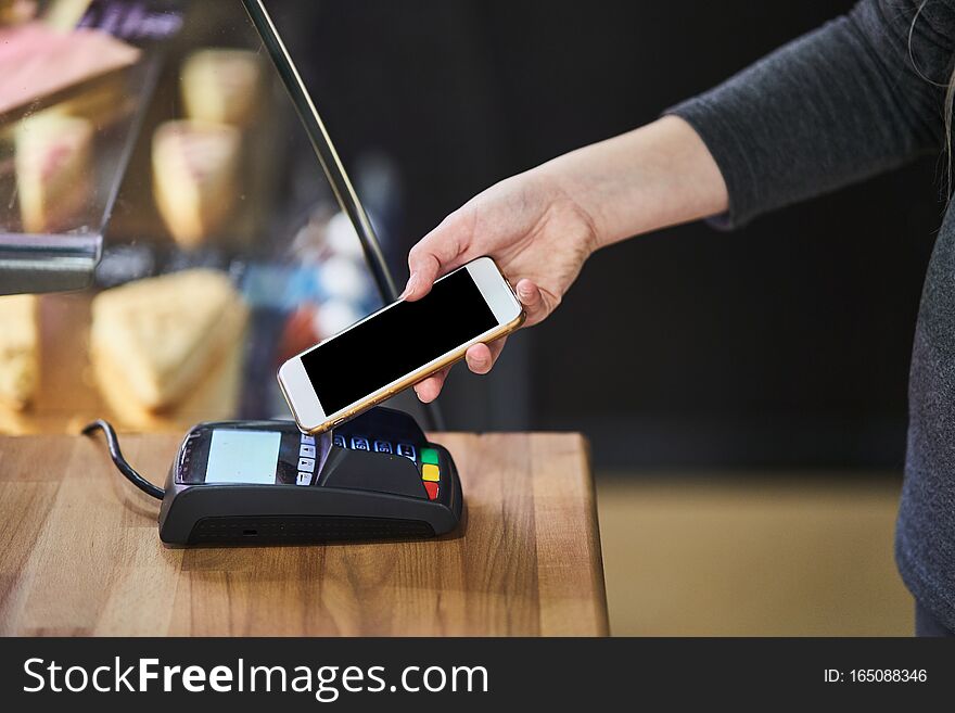 Contactless payment method. The girl applies the phone to the banking terminal. Female customers using the cell phone to pay for goods. Contactless payment method. The girl applies the phone to the banking terminal. Female customers using the cell phone to pay for goods.