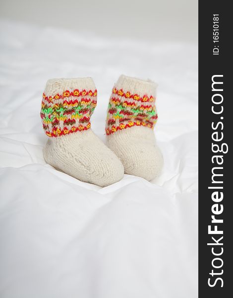 Tine knitted baby bootees on white blanket. Tine knitted baby bootees on white blanket