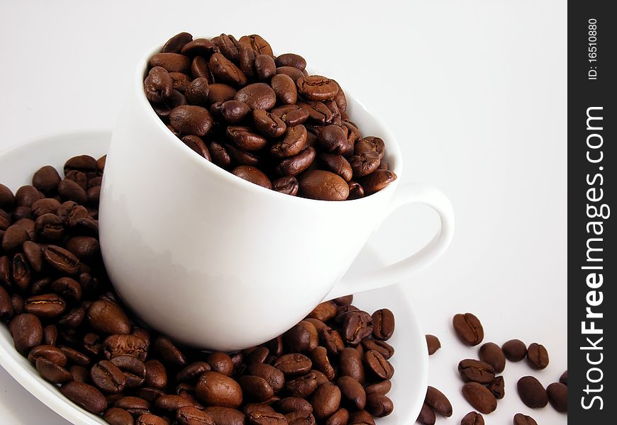 A white coffee cup surrounded with fresh coffee beans. A white coffee cup surrounded with fresh coffee beans