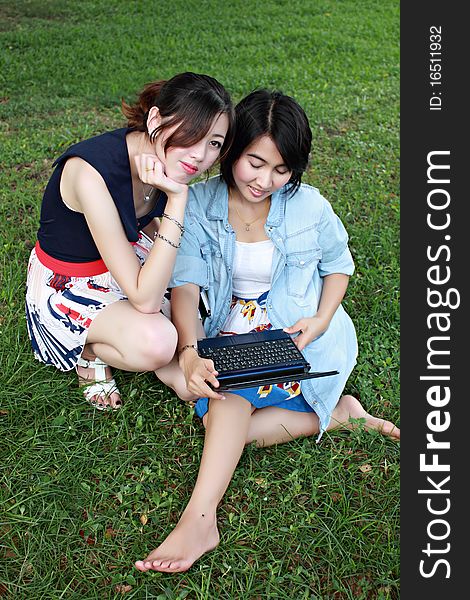 Two beautiful girl with a laptop computer outdoors. Lay on the green grass. Two beautiful girl with a laptop computer outdoors. Lay on the green grass.