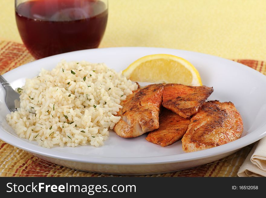 Tilapia fish fillets dinner with with rice, a lemon slice and a drink. Tilapia fish fillets dinner with with rice, a lemon slice and a drink