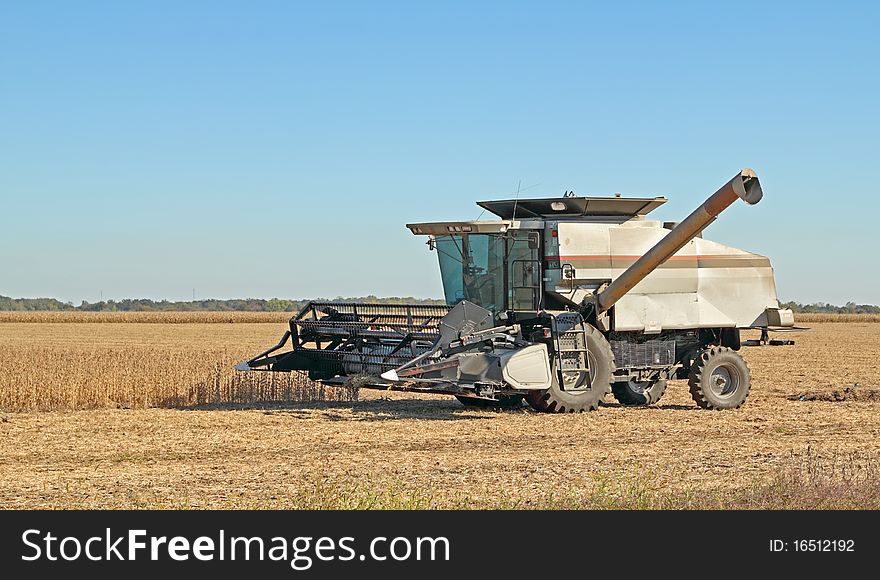 Combine in a farm field harvesting soybeans with a clear blue sky. Combine in a farm field harvesting soybeans with a clear blue sky