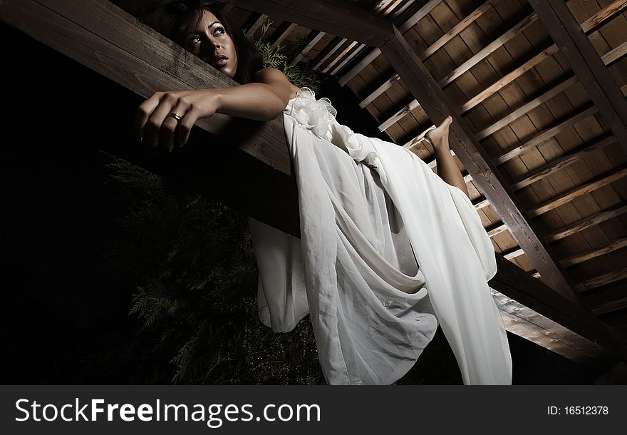 Attractive suntanned girl in white dress poses on a wooden beam. Attractive suntanned girl in white dress poses on a wooden beam.