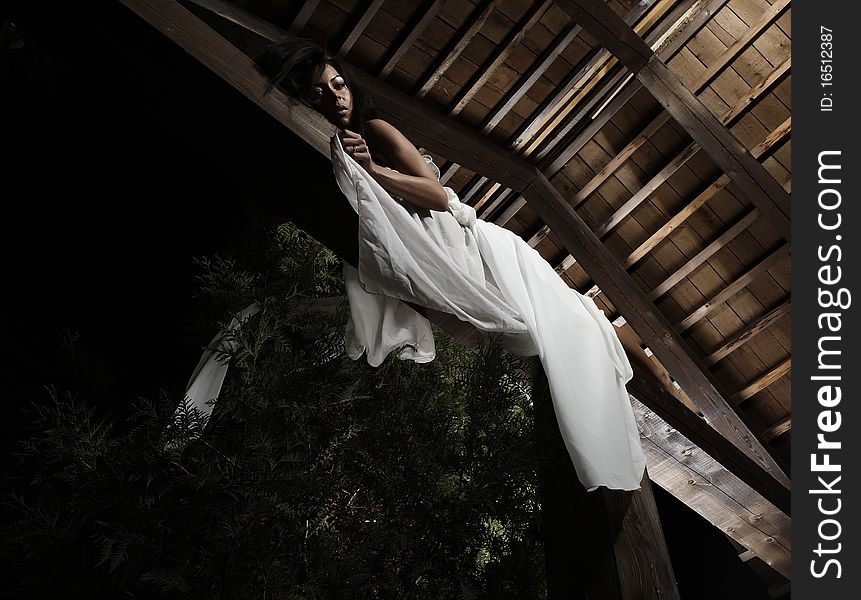 Attractive suntanned girl in white dress poses on a wooden beam. Attractive suntanned girl in white dress poses on a wooden beam.