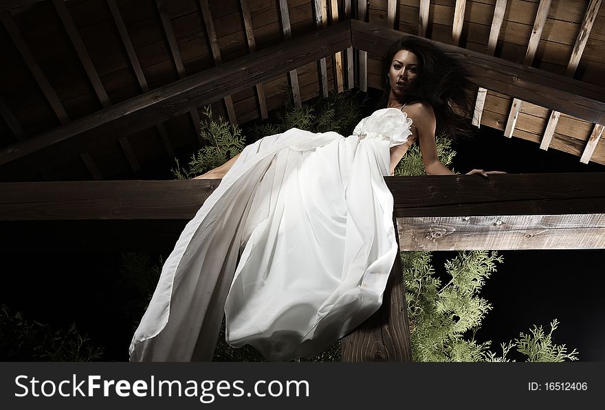 Attractive suntanned girl in white dress poses on a wooden beam. Attractive suntanned girl in white dress poses on a wooden beam.