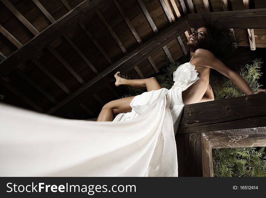 Attractive suntanned girl in white dress poses on a wooden beam. Attractive suntanned girl in white dress poses on a wooden beam.