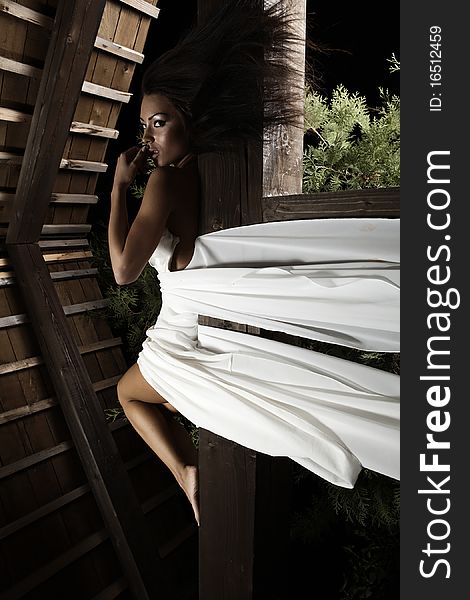 Attractive suntanned girl in white dress poses on a wooden beam. Attractive suntanned girl in white dress poses on a wooden beam.