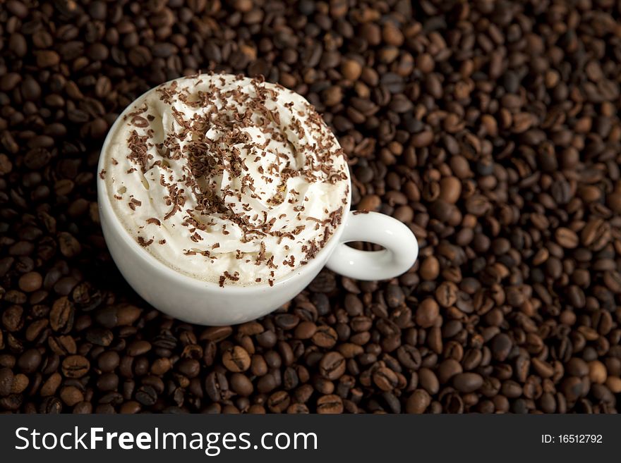 Coffee cup with cream in a pile of coffee beans