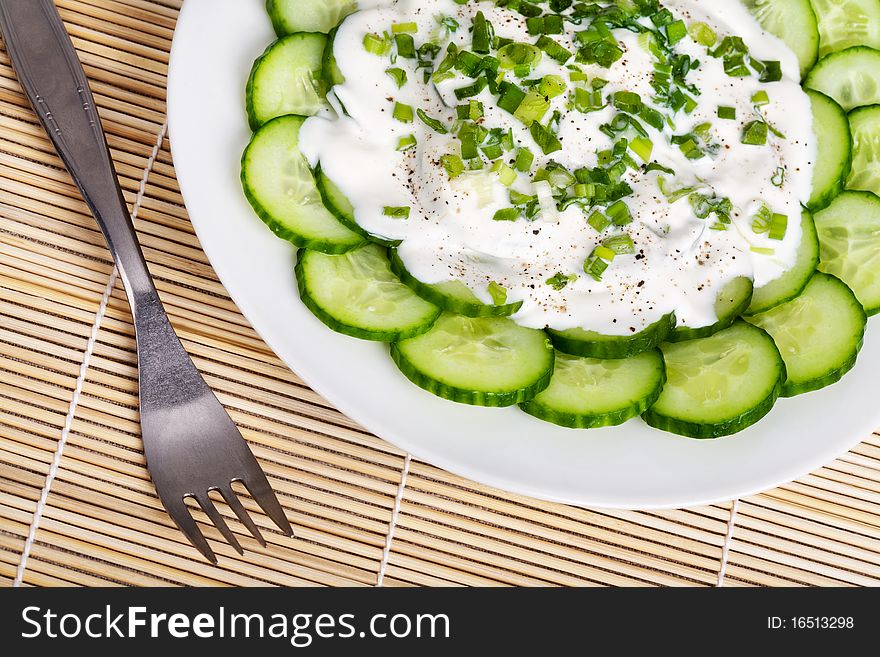 Fresh cucumber slices with sour cream and green onion on a plate