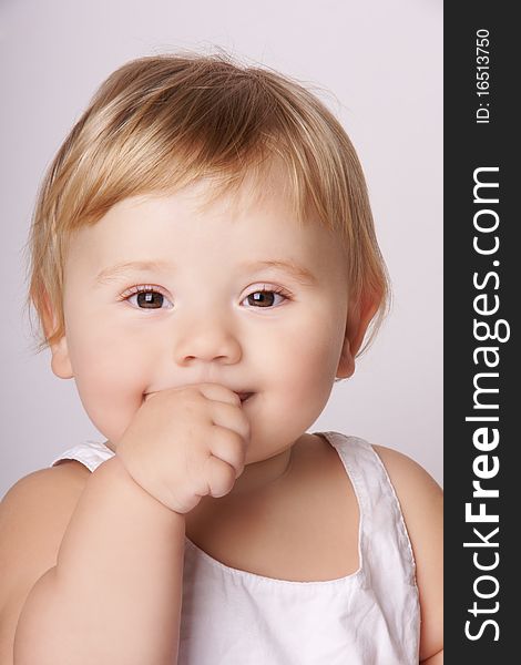 Portrait of happy smiling pretty baby holding finger in mouth, studio shot