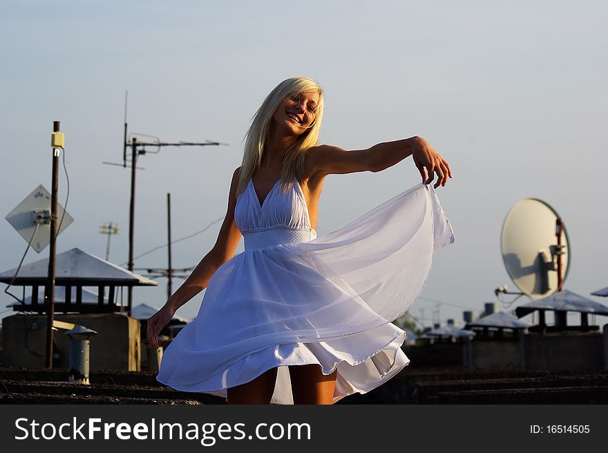 Pretty girl is posing on the roof with white beautiful dress. She is dancing because she likes the good weather. Pretty girl is posing on the roof with white beautiful dress. She is dancing because she likes the good weather.
