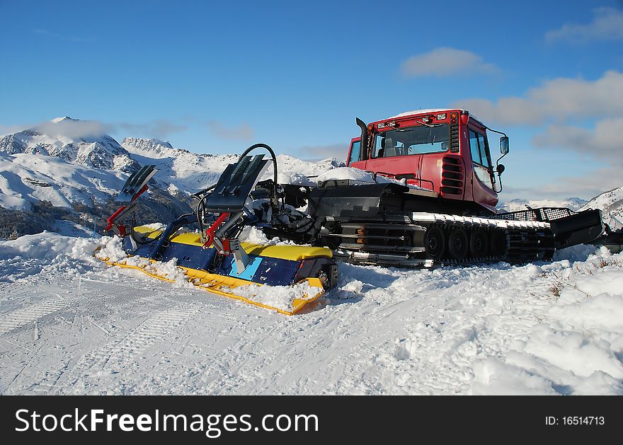 We can see a tractor in the middle of a mountain, full of snow, in the pyrenees, in France, (el Formigal). This is the tractor who prepare the tracks for skiing. In the background we can see mountains and the blue sky, with some grey clouds. We can see a tractor in the middle of a mountain, full of snow, in the pyrenees, in France, (el Formigal). This is the tractor who prepare the tracks for skiing. In the background we can see mountains and the blue sky, with some grey clouds.