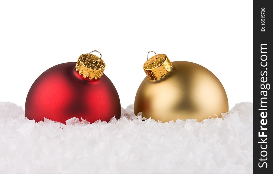 Red and gold Christmas baubles sitting in the snow.