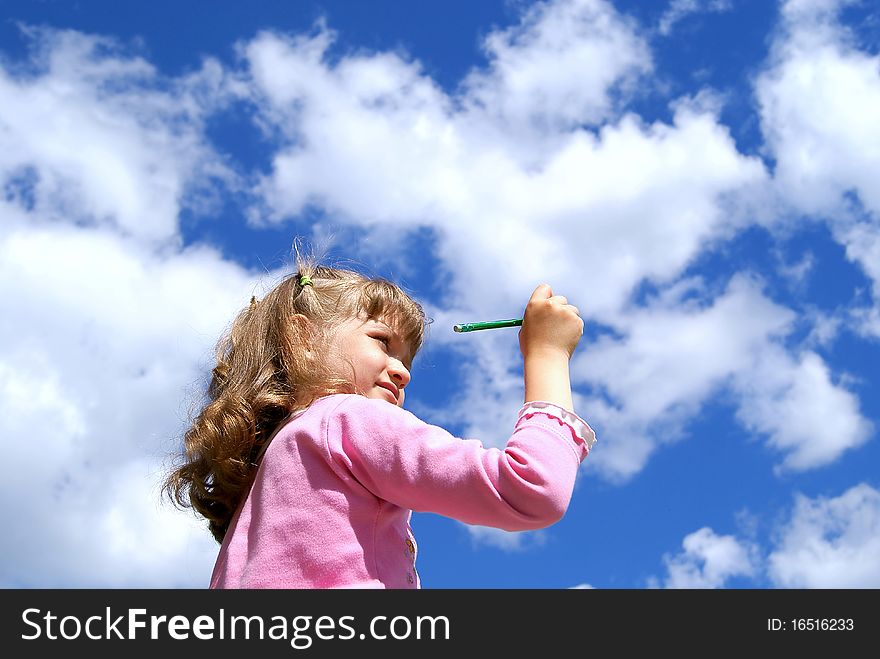 The girl draws a green pencil in the blue sky with white clouds in the summer. The girl draws a green pencil in the blue sky with white clouds in the summer