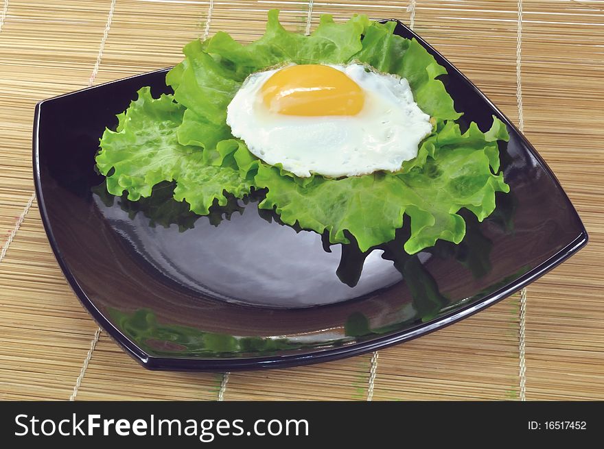 Fried eggs and lettuce leaves on a black plate