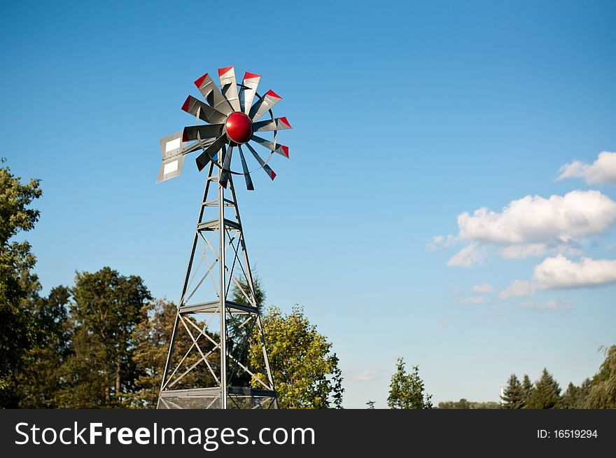 A small windmill spins with blue sky and clouds in the background. A small windmill spins with blue sky and clouds in the background