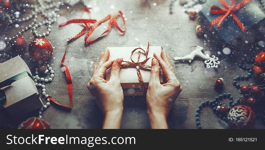 Christmas New Year concept top view. Unrecognizable woman wrapping draws a gift box on wooden table with snow and bokeh, point of