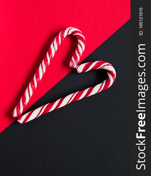 Red candy canes folded in the form of a heart on a contrasting red and black background. Top View. Photo for your postcard. Festive concept for New Year and Christmas. Red candy canes folded in the form of a heart on a contrasting red and black background. Top View. Photo for your postcard. Festive concept for New Year and Christmas