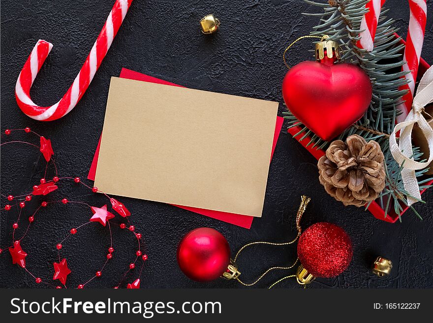 Red gift box with a Christmas toy in the shape of a heart, fir branches, christmas candy, garland and card for congratulatory text