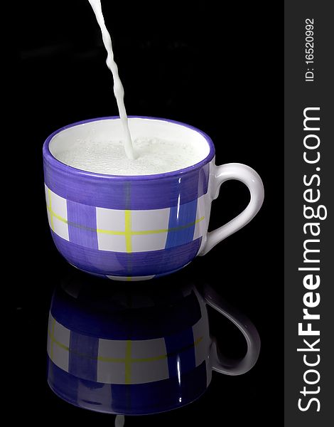 Fresh milk with foam being poured to the blue and white cup on the black backgraund. Fresh milk with foam being poured to the blue and white cup on the black backgraund