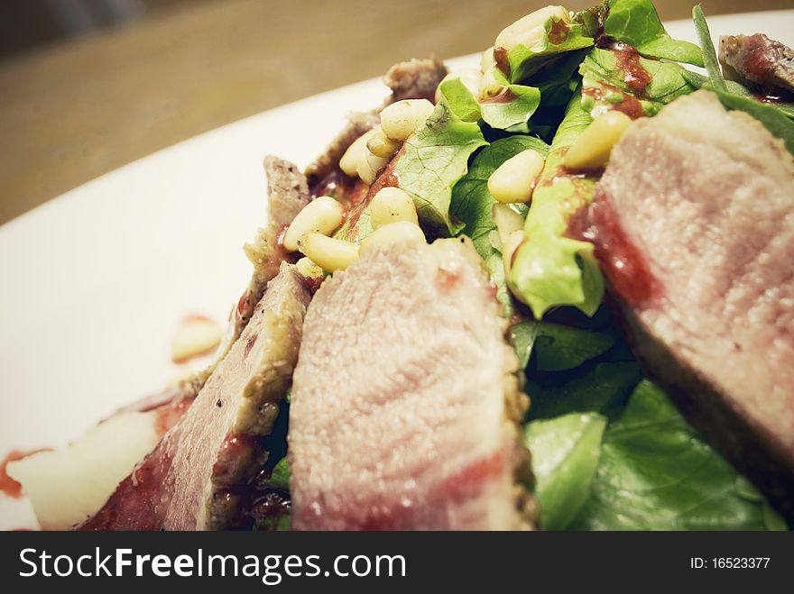 Meat with salad and nuts served on the white plate. Meat with salad and nuts served on the white plate