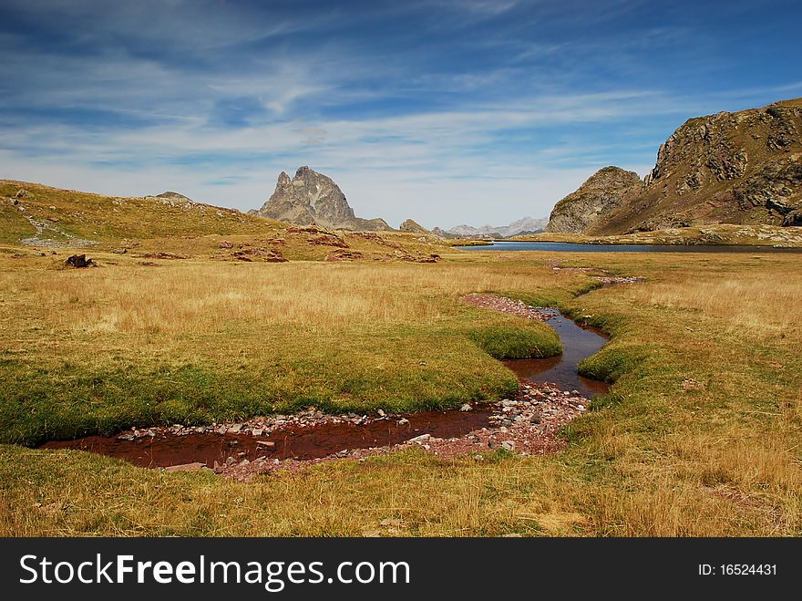 Panorama of Anayet plateau with a small stream red from rocks in Spanich Aragon and Peak du Midi d'Ossau in French Bearn in Pyrenees mountains at background,  in summer time. Panorama of Anayet plateau with a small stream red from rocks in Spanich Aragon and Peak du Midi d'Ossau in French Bearn in Pyrenees mountains at background,  in summer time