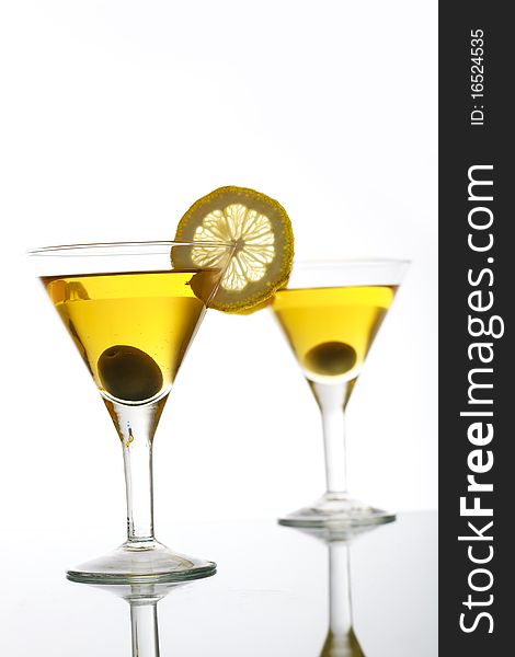 Two glasses with classical martini on reflection surface, garnished olive and lemon. Two glasses with classical martini on reflection surface, garnished olive and lemon.