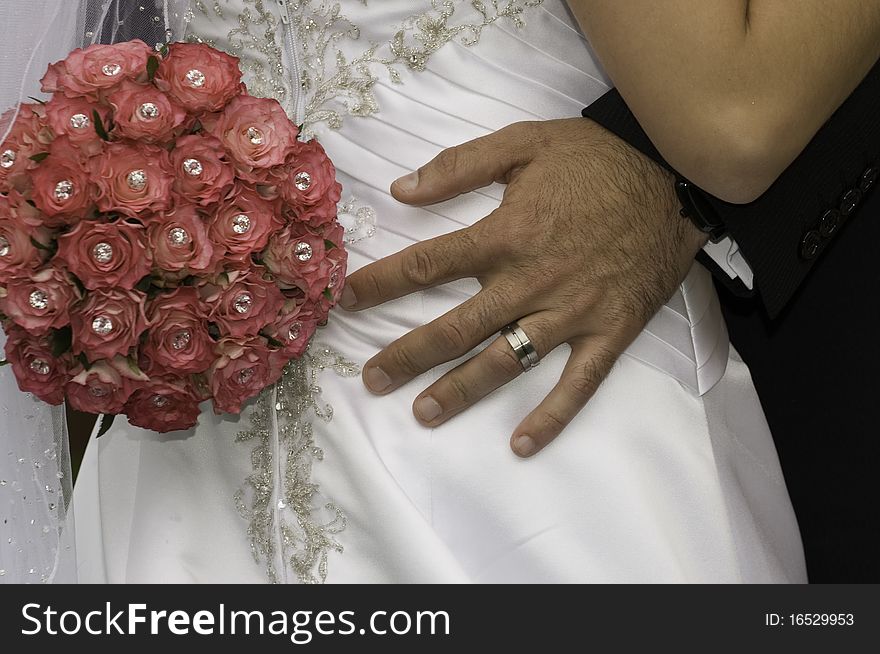 Groom standing with his hand wearing a wedding ring and red bouquet on his brides. Groom standing with his hand wearing a wedding ring and red bouquet on his brides