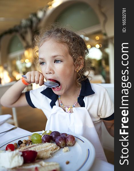 Cute little girl with curly hair eats a cake at the restaurant with widely open mouth. Cute little girl with curly hair eats a cake at the restaurant with widely open mouth