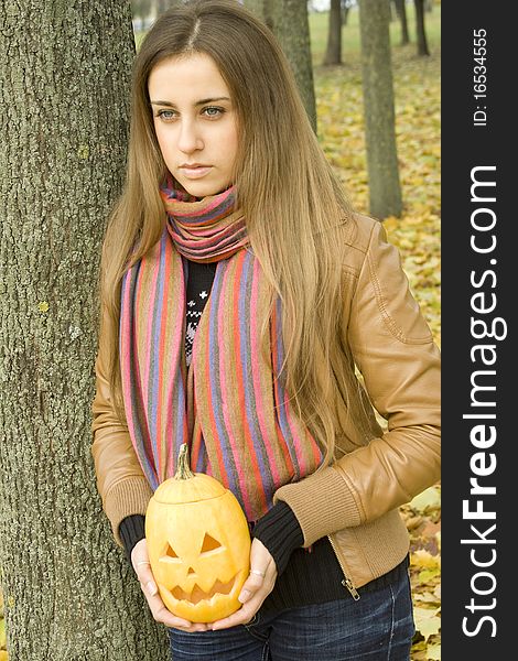 Young girl outdoors in autumn in the park with a pumpkin for Halloween