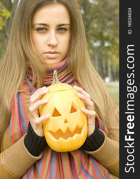 Young girl outdoors in autumn in the park with a pumpkin for Halloween
