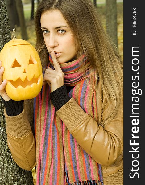 A young girl frightened with pumpkin for Halloween. Gesturing for Quiet or Shushing. Autumn on the street. A young girl frightened with pumpkin for Halloween. Gesturing for Quiet or Shushing. Autumn on the street