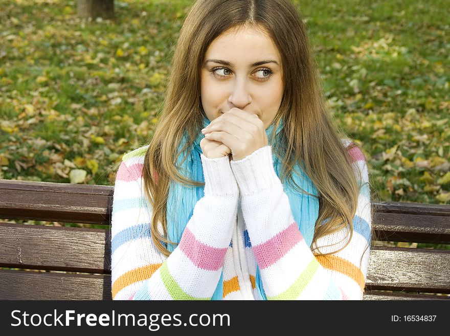 Vertical portrait of a beautiful young woman sitting on a bench in the park around a lot of yellow, red green leaves. Breath warms your hands. Vertical portrait of a beautiful young woman sitting on a bench in the park around a lot of yellow, red green leaves. Breath warms your hands