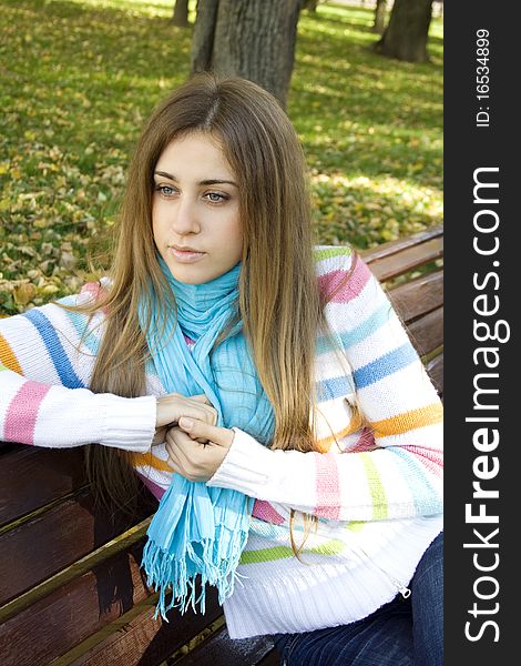 Portrait of a beautiful young woman sitting on a bench in the park around a lot of yellow, red green leaves. Portrait of a beautiful young woman sitting on a bench in the park around a lot of yellow, red green leaves.