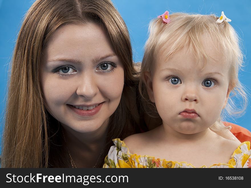 Young and beautiful mother with her sweet little daughter isolated on blue. Young and beautiful mother with her sweet little daughter isolated on blue.