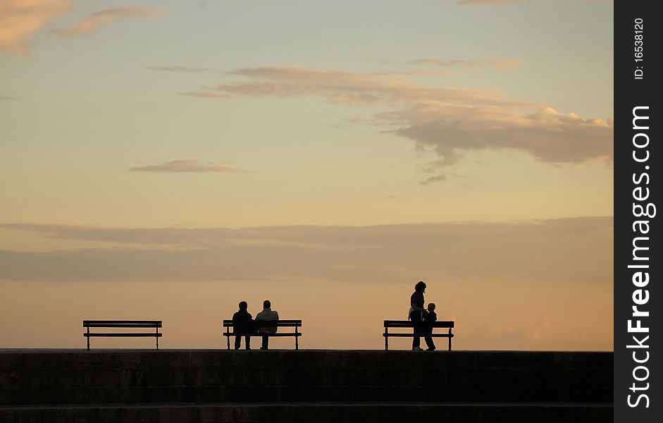 Silhouettes over sunset - pair on one bench and mother with child near another