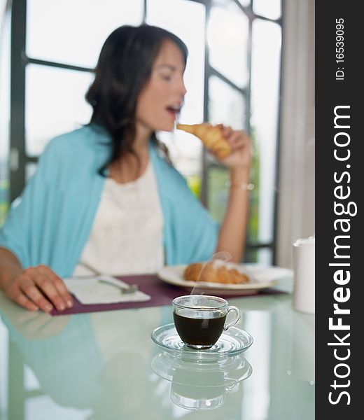 Mid adult woman eating croissant at home. Vertical shape, copy space, focus on cup of coffee. Mid adult woman eating croissant at home. Vertical shape, copy space, focus on cup of coffee