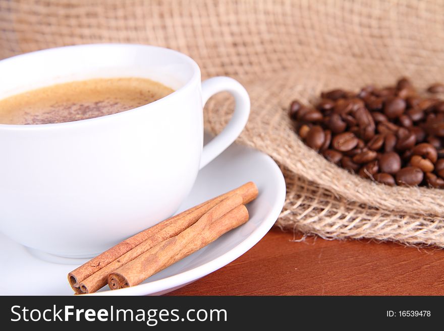 Cup of coffee sprinkled with cinnamon and with cinnamon sticks, coffee beans and burlap material. Cup of coffee sprinkled with cinnamon and with cinnamon sticks, coffee beans and burlap material